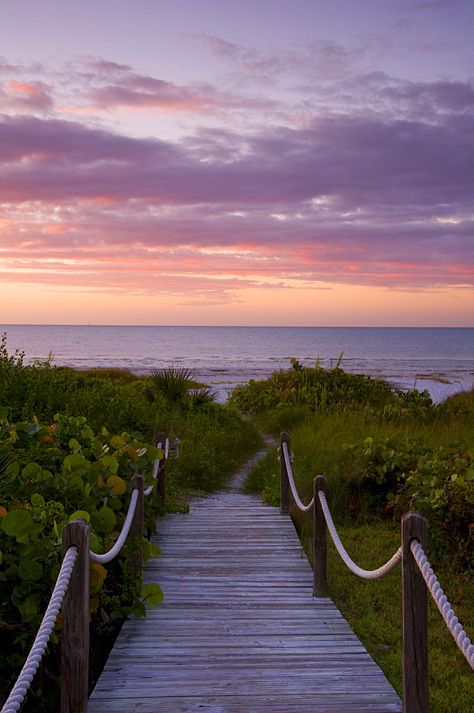 A boardwalk over sand dunes and tropical vegetation leading to the beach at sunrise, Sanibel Island, Florida, United States of America, North America