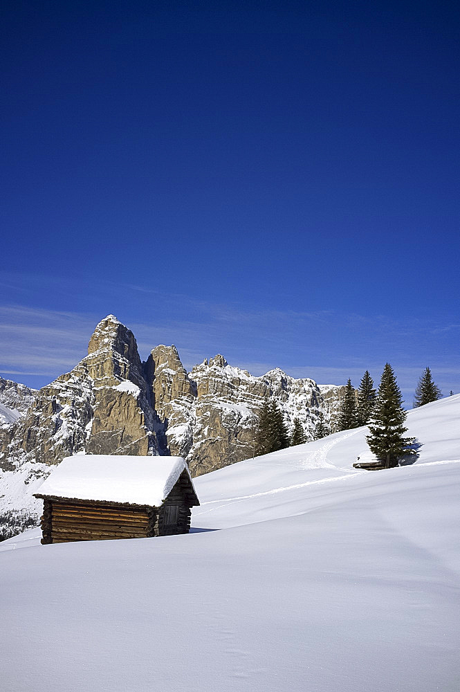 A snow covered wooden barn at the Alta Badia ski resort and Sassongher mountain behind, Corvara, The Dolomites, South Tyrol, Italy, Europe