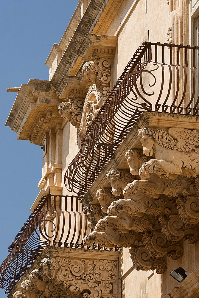 Baroque stone carvings of heads under a balcony at the Palazzo Nicolaci di Villadorata in Noto, UNESCO World Heritage Site, Syracuse Province, Sicily, Italy, Europe