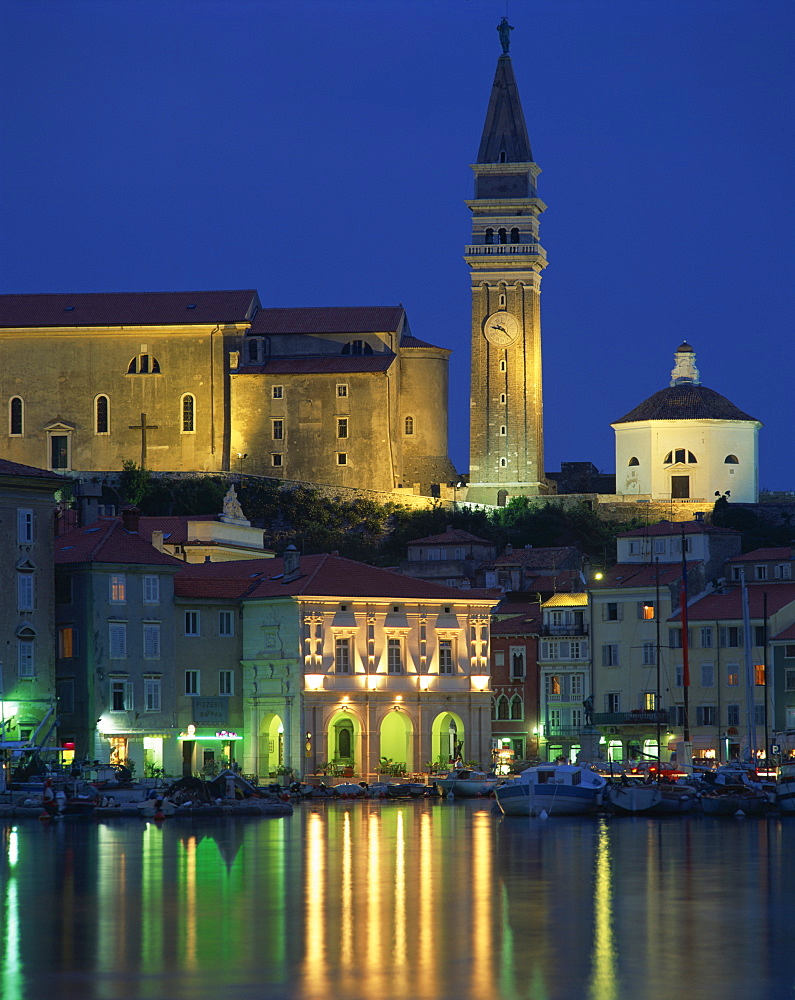 Waterfront buildings, clock tower and church at night on the harbour at Piran, Slovenia, Europe