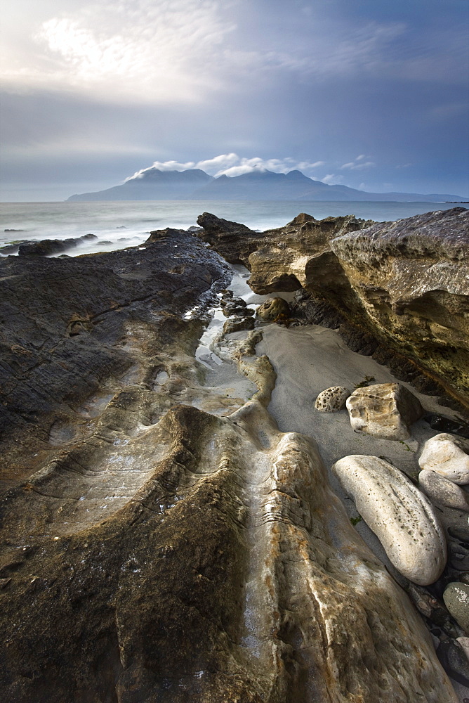 Looking towards Isle of Rum at twilight from rocks at Singing Sands (Camas Sgiotaig), Isle of Eigg, Inner Hebrides, Scotland, United Kingdom, Europe