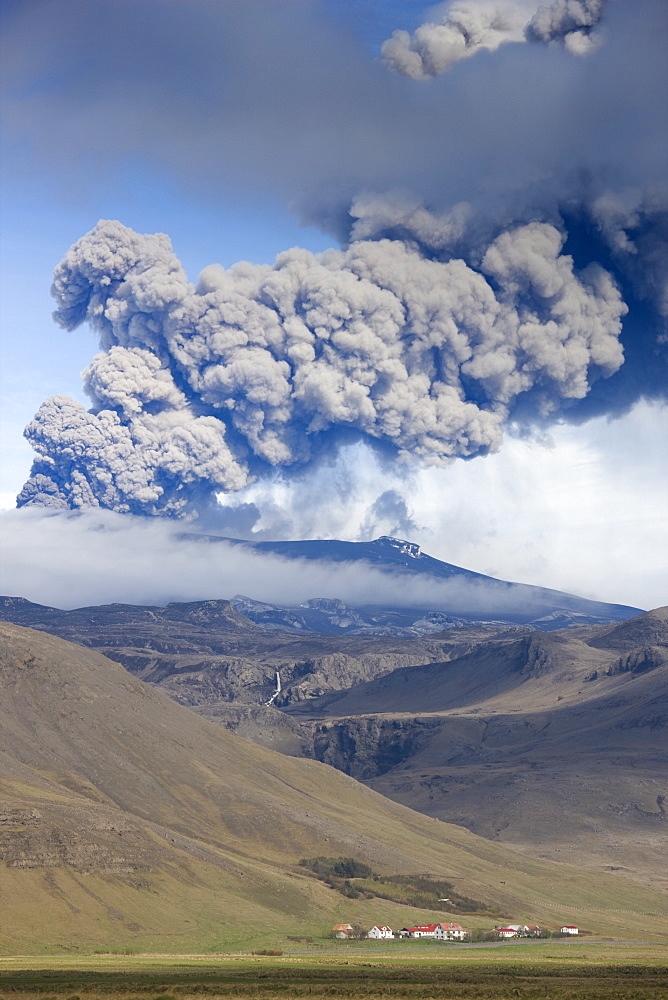 Houses at foot of mountains with the ash plume of the Eyjafjallajokull eruption in the distance, southern area, Iceland, Polar Regions