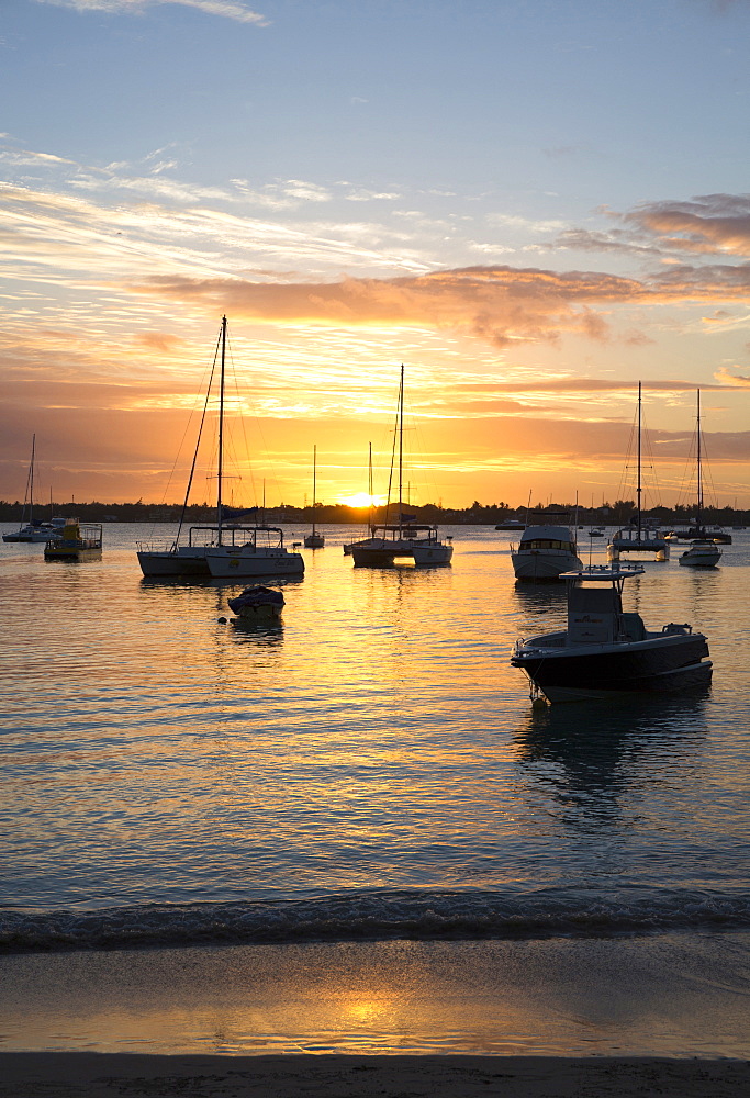 Sunset over the Indian Ocean with boats in silhouette on the calm water off the beach at Gran Baie on the north coast of Mauritius, Indian Ocean, Africa