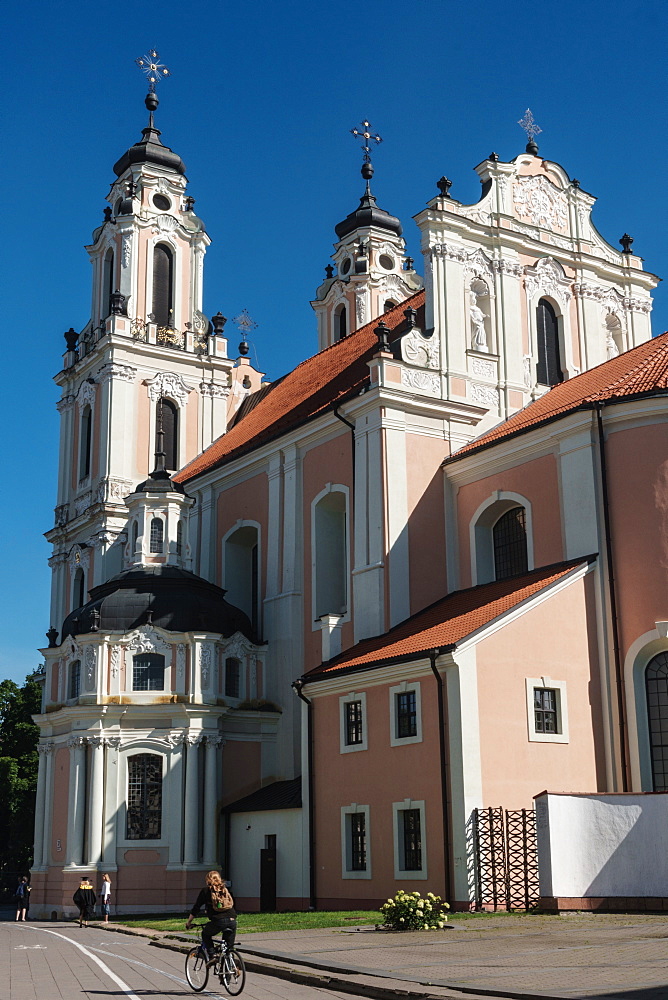 Cyclist passes by strawberry and cream Baroque Church of St Catherine, Old Town, UNESCO Wolrd Heritage Site, Vilnius, Lithuania, Europe