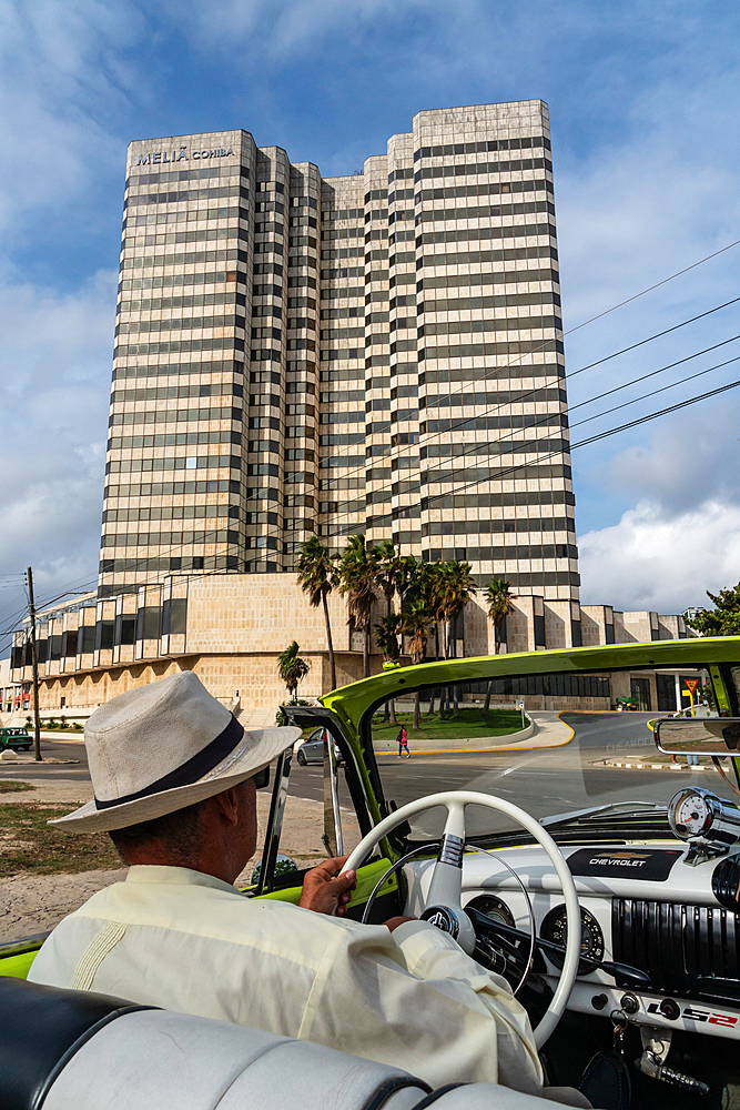 Driver with panama hat in green open top Chevrolet classic car driving through city, Havana, Cuba (Model Release)