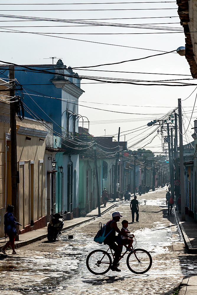 Typical backstreet under panoply of telephone wires, silhouetted family on bike, Trinidad, Cuba