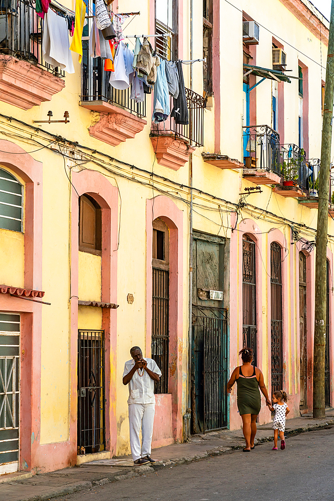 Man lights cigar in typical backstreet, colourful washing draped on balconies, Old Havana, Cuba 2