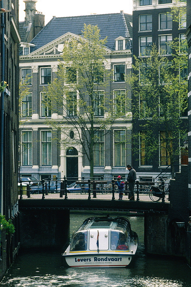 Netherlands, Amsterdam, Tour Boat Passing Under A Narrow Bridge On A Canal