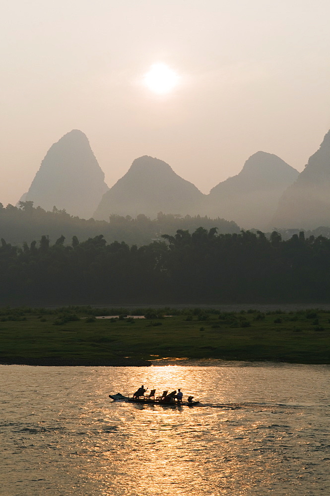 Tourist boat sailing through karst scenery at sunrise on the Li river (Lijiang) in Yangshuo, near Guilin, Guangxi Province, China, Asia