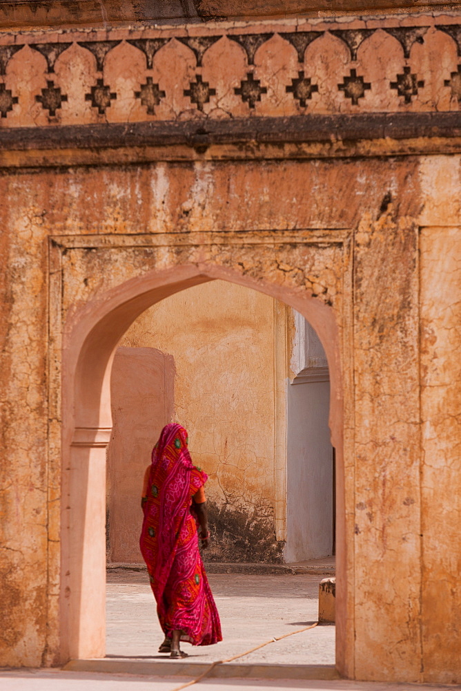 Lady in traditional dress walking through a gateway in the Amber Fort near Jaipur, Rajasthan, India, Asia