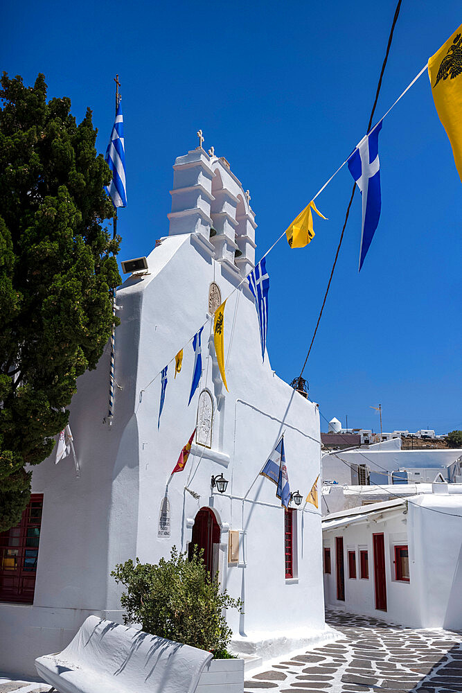 Saint George Church and flags on a quaint street in Mykonos Old Town, Mykonos, The Cyclades, Aegean Sea, Greek Islands, Greece, Europe