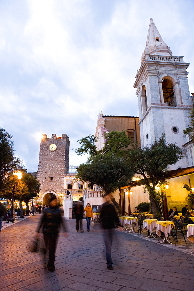 People strolling in Piazza IX Aprile in the evening, with the Torre dell Orologio and San Giuseppe church, Taormina, Sicily, Italy, Europe