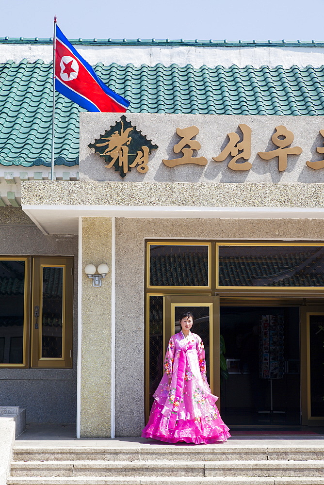 Woman in colourful traditional dress at entrance to tourist shop, Democratic People's Republic of Korea (DPRK), North Korea, Asia