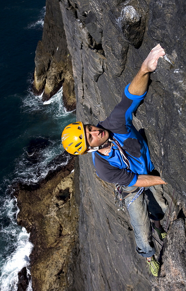 A climber makes his way up the huge vertical sea cliff on the west face of Dun Mingulay, Mingulay Island, near Barra and Lewis, Outer Hebrides, Scotland, United Kingdom, Europe