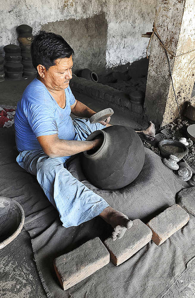 Man beating hand made charcoal dusted terracotta water jar into traditional shape with a wooden paddle, Chhote Udepur, Gujarat, India, Asia