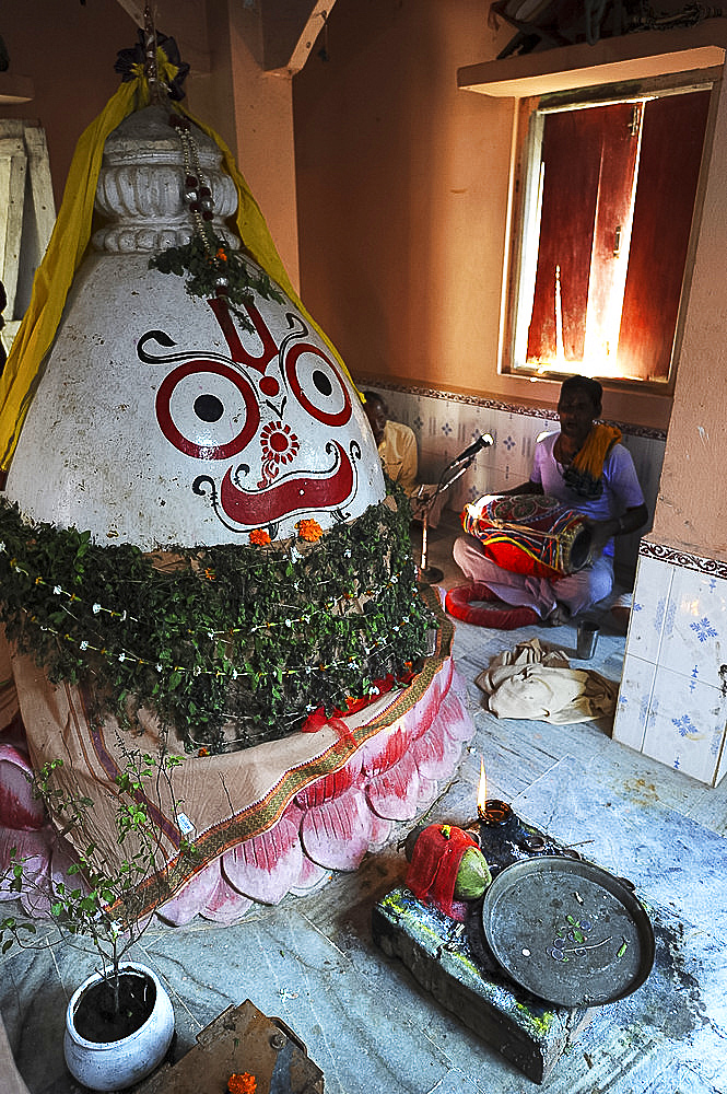 Musician plays the drum at the shrine to Lord Jagannath inside the village temple, rural Odisha, India, Asia