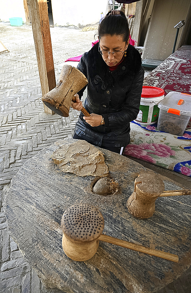 Uyghur woman beating boiled Mulberry bark with wooden mallet for paper making, Hotan, China, Asia