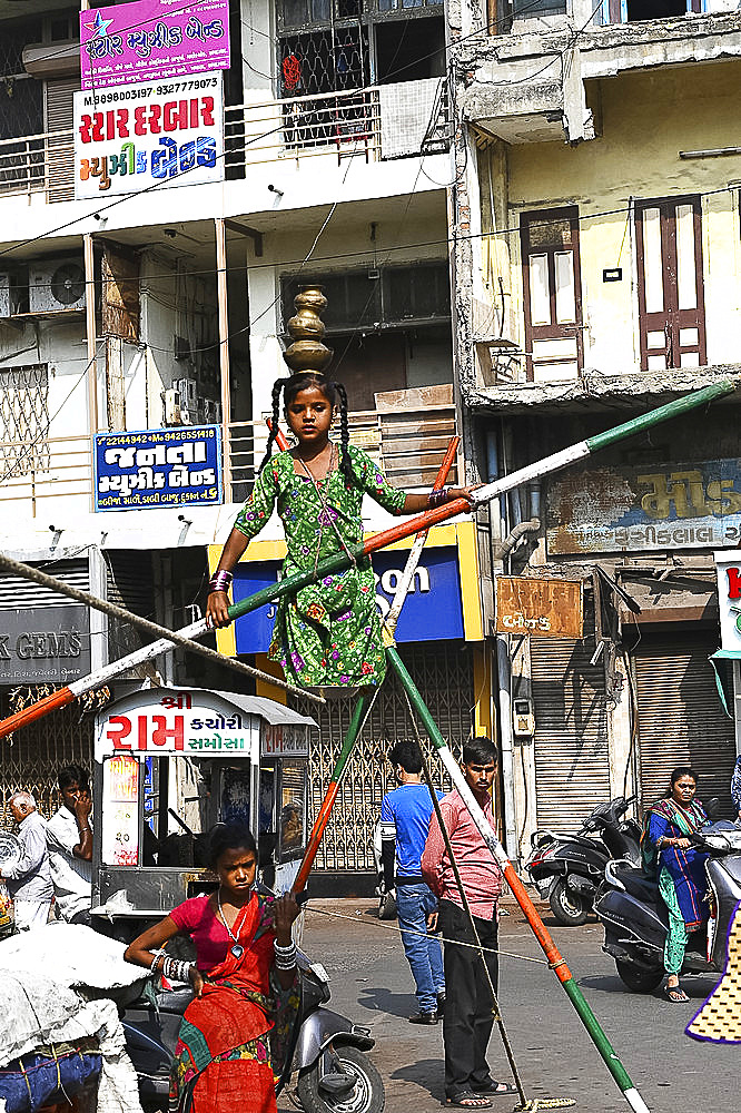 Young girl performing on a tightrope erected in a busy street to earn money, old Ahmedabad, Gujarat, India, Asia