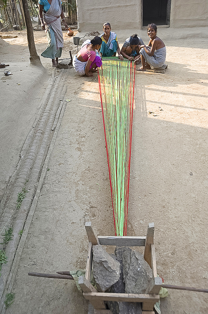 Village women in village communal area preparing sari length of coloured cotton for weaving, Ganeshpahar village, Assam, India