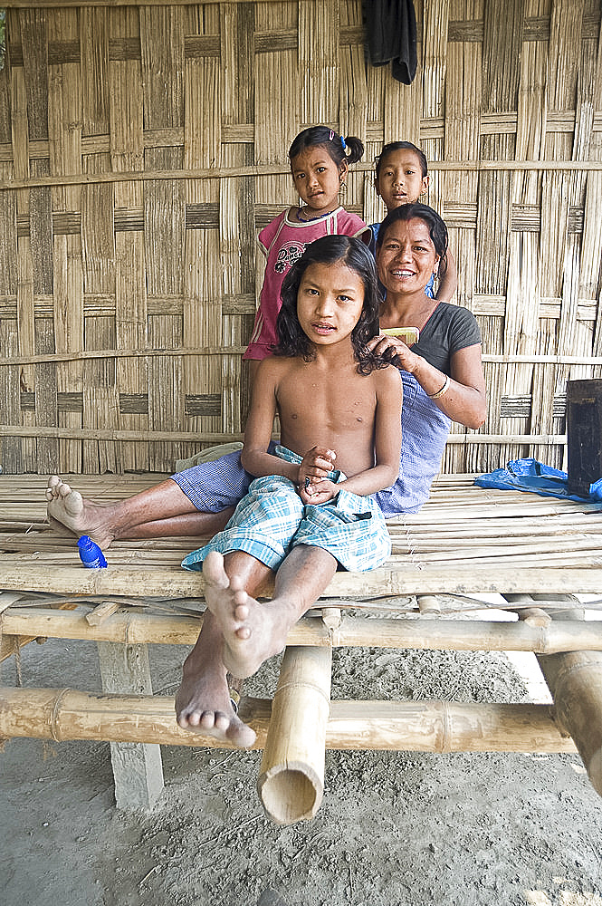 Mishing tribeswoman combing her daughter's hair on the verandah of their family home, Majuli Island, Assam, India, Asia