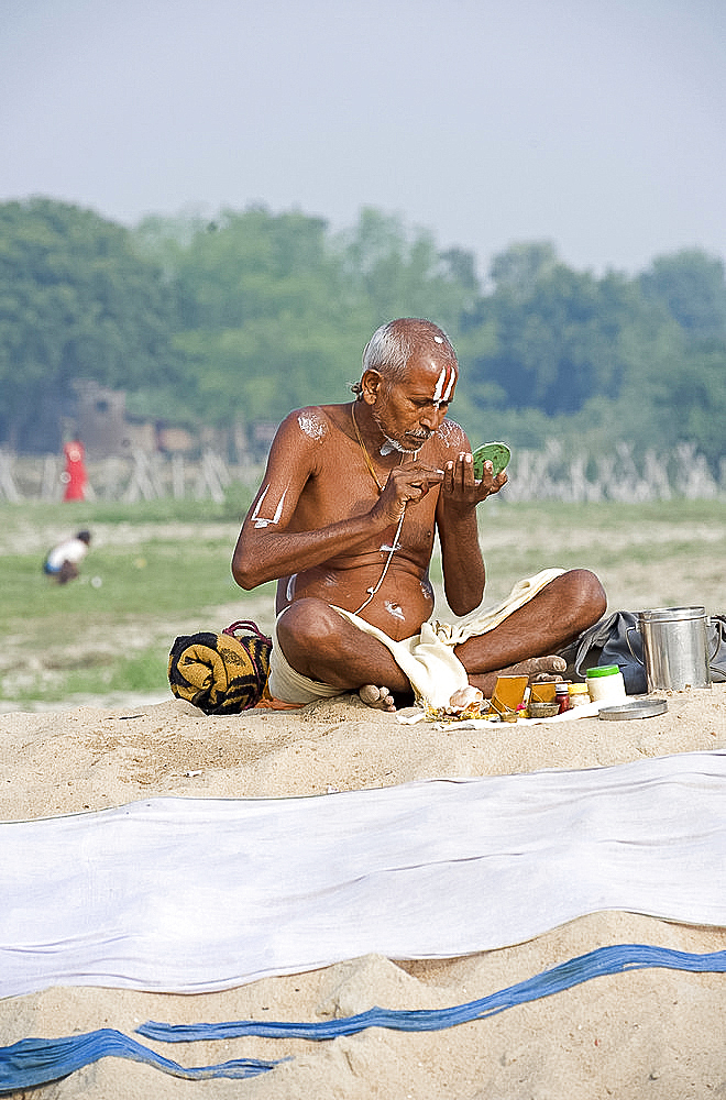 Vishnaivite holy man sitting cross legged, preparing for morning puja, applying sandalwood tilaks on forehead and arms, wearing simple white dhoti and sacred Hindu string, Patna, Bihar, India, Asia