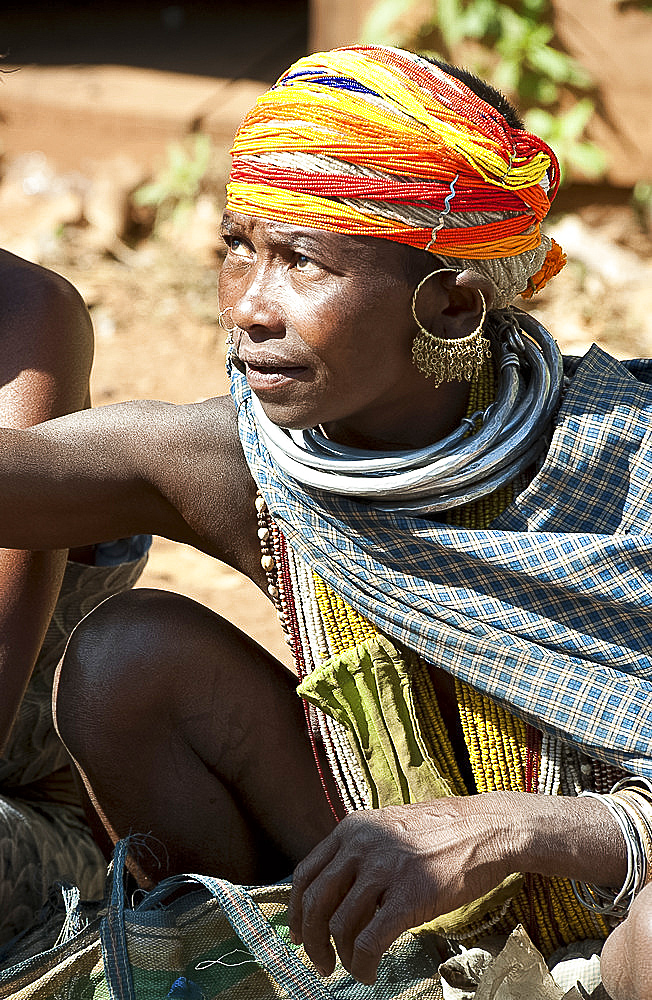 Bonda tribeswoman in traditional dress with beaded cap, large earrings and metal necklaces selling vegetables at weekly market, Rayagader, Orissa, India, Asia