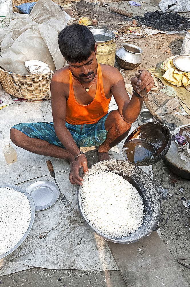 Man in vest and dhoti pouring sugar syrup onto bowl of puffed rice to make prasad, Sonepur Cattle Fair, Bihar, India, Asia