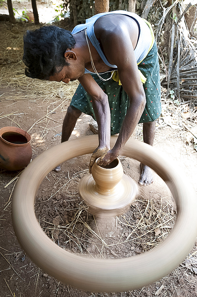 Village potter forming hand made clay pot on potter's wheel spinning in his village workshop, near Rayagada, Orissa, India, Asia