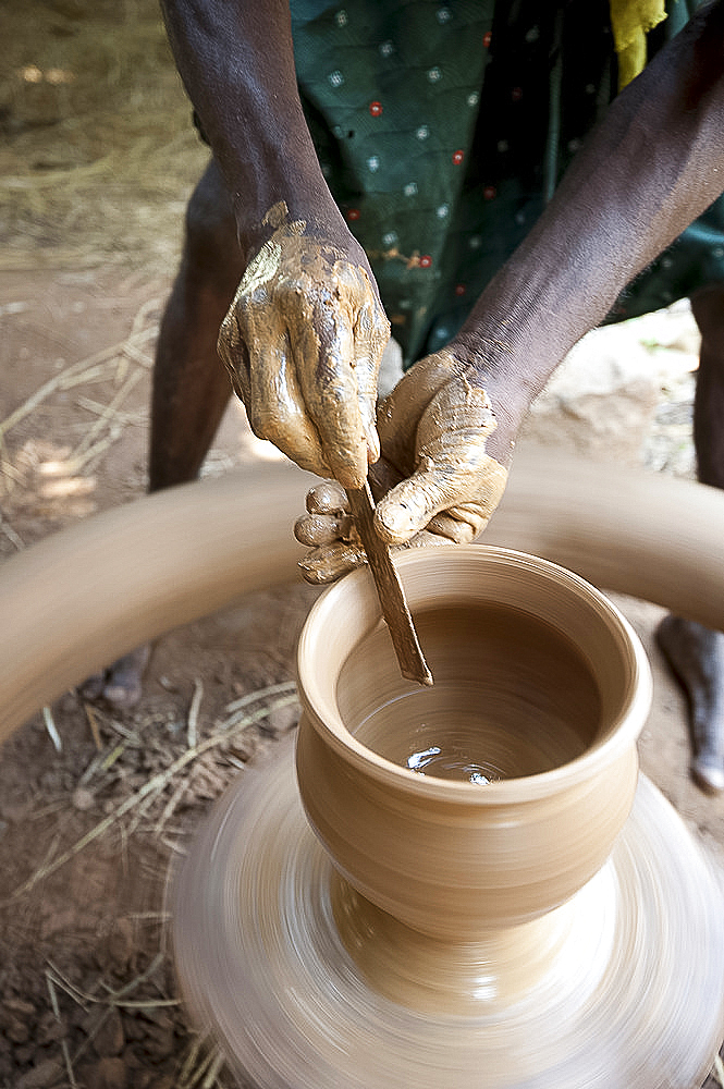 Hands of village potter using tool to shape clay pot on spinning wheel in his village workshop, near Rayagada, Orissa, India, Asia