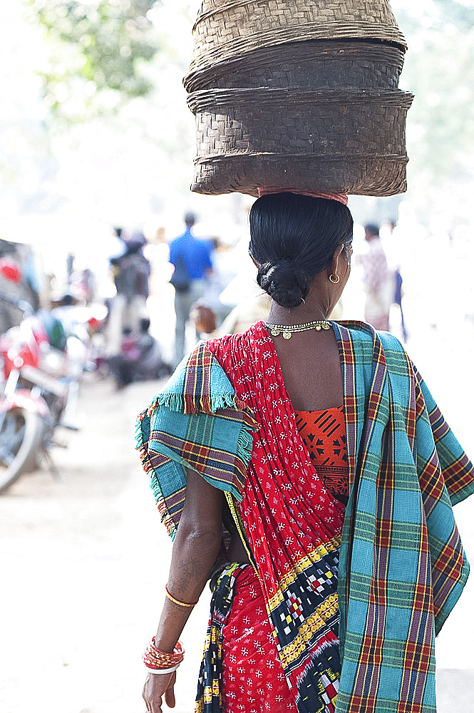 Woman at weekly tribal market wearing brightly coloured clothing and carrying baskets on her head, Bissam Cuttack, Orissa, India, Asia