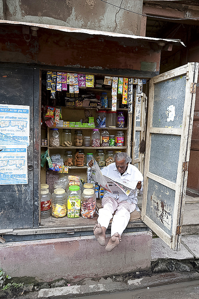 Shop owner reading the newspaper in the morning, Kolkata, West Bengal, India, Asia