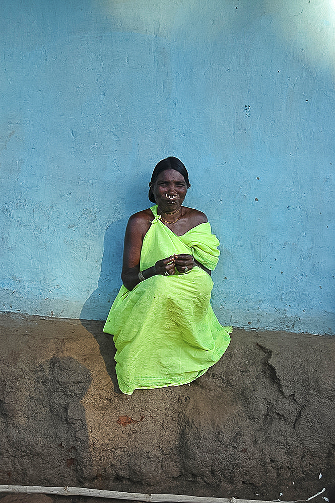 Woman sitting in late afternoon sunshine against blue house wall in Mali tribal village, Jeypore district, Orissa, India, Asia