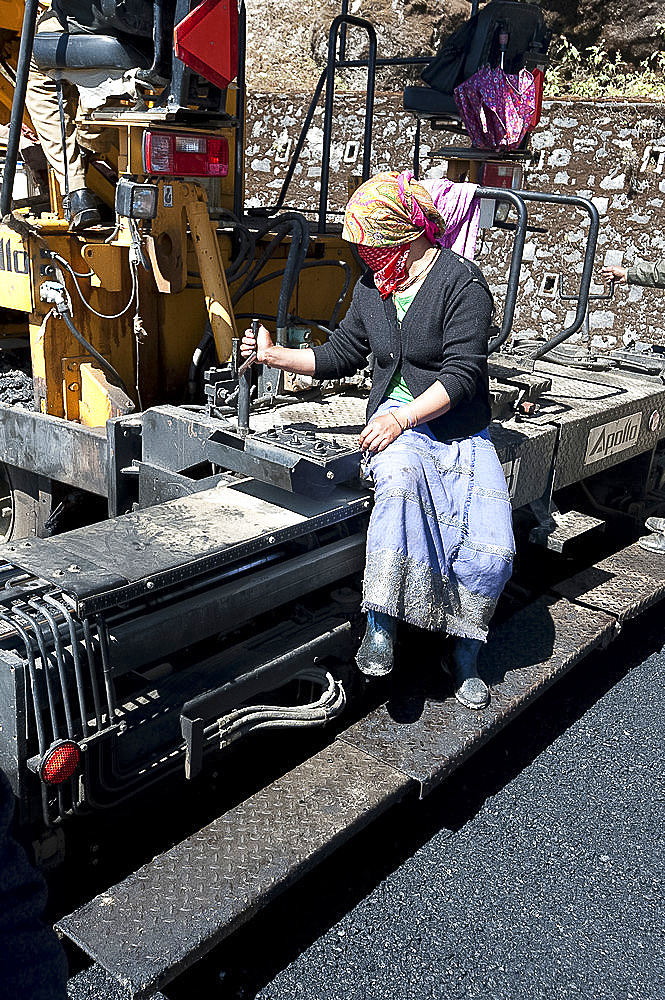 Female road worker in charge of tar spreading machine on hill roads high in Arunachal Pradesh, India, Asia