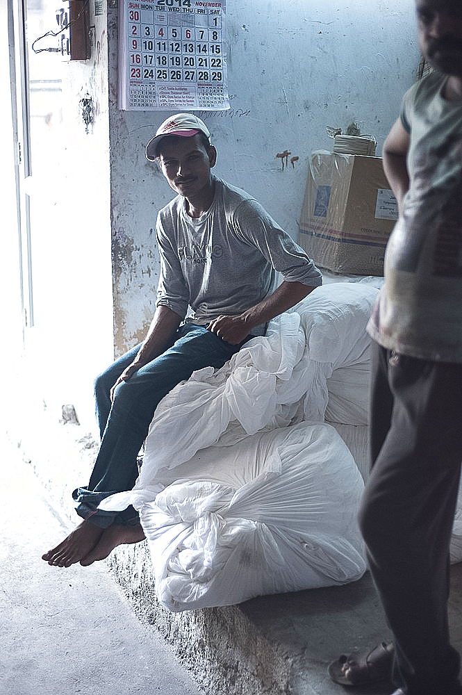 Silkscreen worker pausing from work, sitting on bags of cotton fabric, Bhuj district, Gujarat, India, Asia