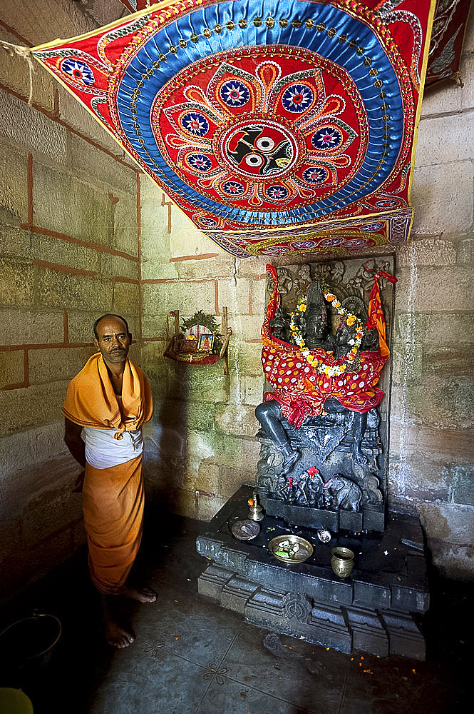 Hindu priest in saffron robes at the Radha Krishna shrine in tiny rural temple, Chaurasi, Prachi Valley, Odisha, India, Asia