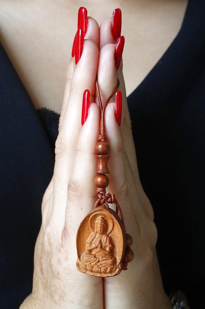 Buddhist woman praying with a wood Buddha pendant in hands, Ho Chi Minh City, Vietnam, Indochina, Southeast Asia, Asia