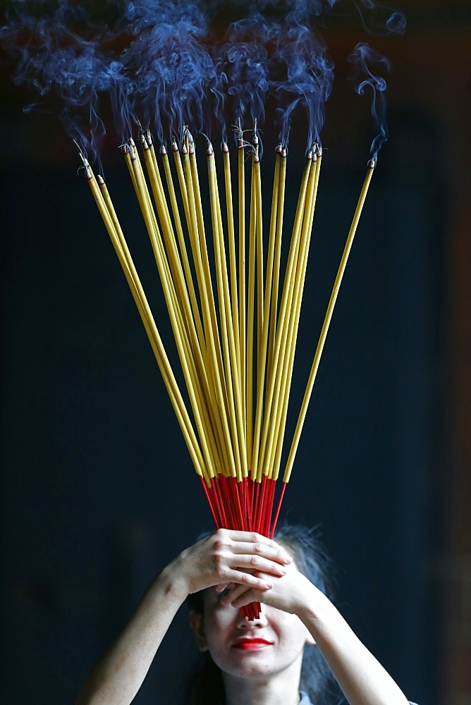 Young Chinese woman praying with big burning incense sticks in her hands, Ha Chuong Hoi Quan Pagoda, Ho Chi Minh City, Vietnam, Indochina, Southeast Asia, Asia