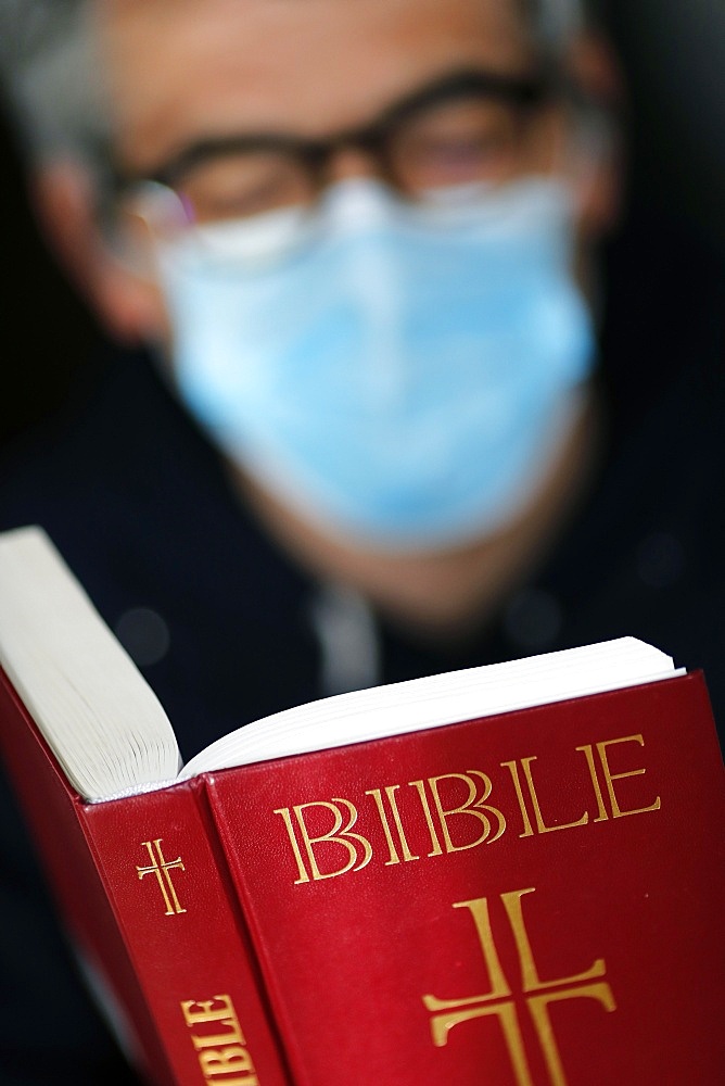 Man reading the bible with a disposable mask to avoid contagious coronavirus (COVID-19), France, Europe