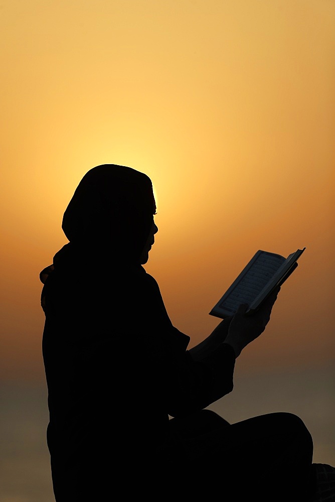 Silhouette of a Muslim woman reading the Noble Quran at sunset, United Arab Emirates, Middle East