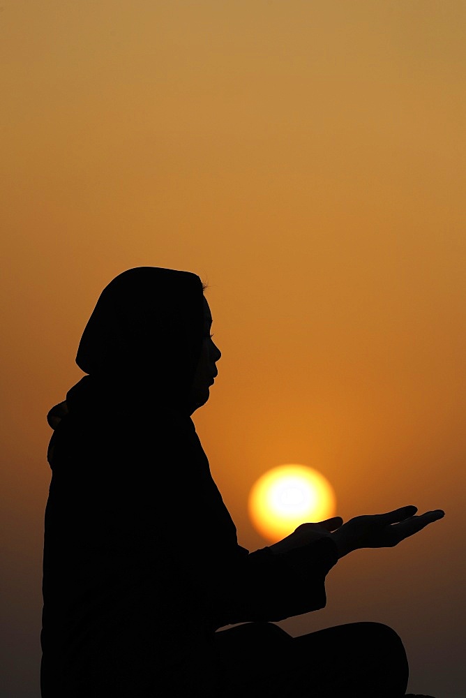 Silhouette of a Muslim woman in abaya praying with her hands at sunset, United Arab Emirates, Middle East