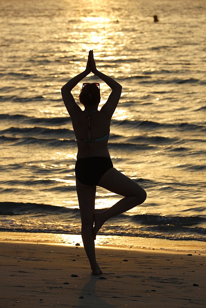 Woman practising yoga meditation on beach at sunset as concept for silence and relaxation, United Arab Emirates, Middle East