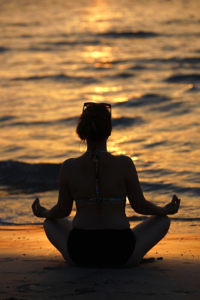 Woman practising yoga meditation on beach at sunset as concept for silence and relaxation, United Arab Emirates, Middle East