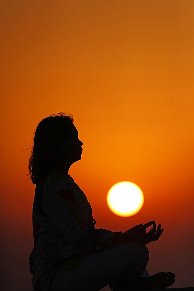 Woman practising yoga pose and meditation at sunset as concept for silence and relaxation, United Arab Emirates, Middle East