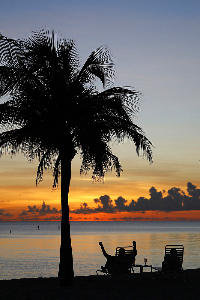 Retired man sitting on a chair at sunset, tropical beach and paradise nature, Cayman Islands, Caribbean, Central America