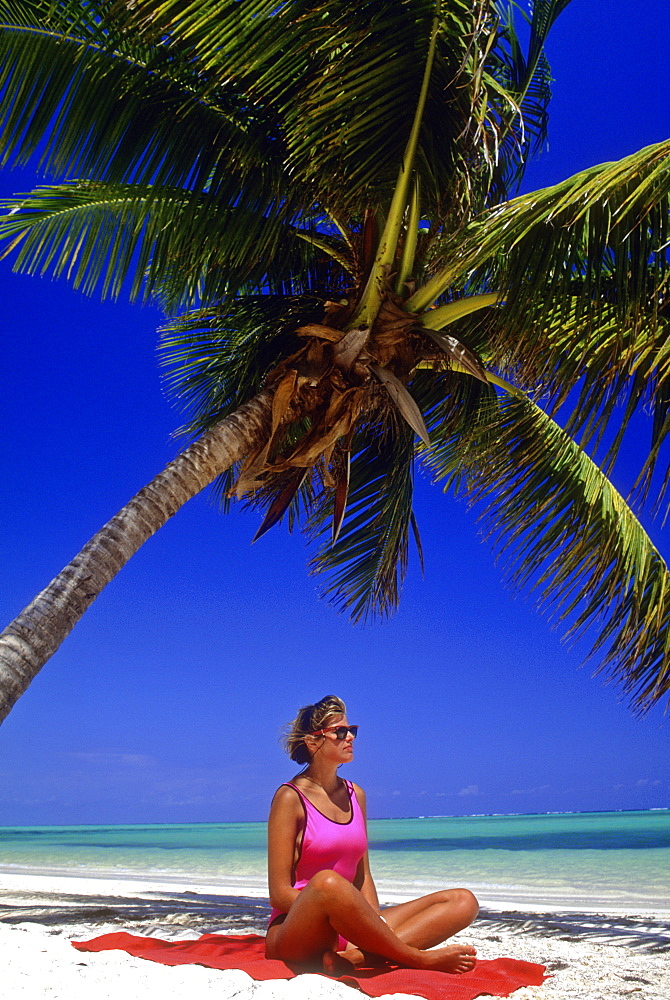 Young woman sitting under a palm tree facing the Caribbean Sea, Bavaro Beach, Punta Cana, Dominican Republic, West Indies, Caribbean, Central America