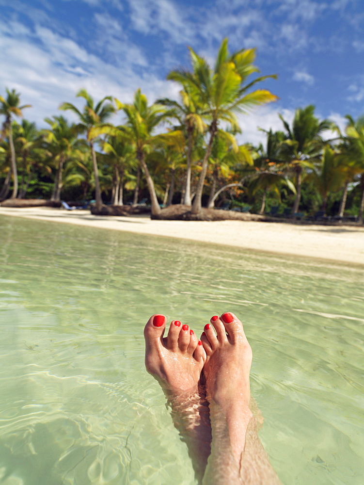 Woman's feet floating in water against a palm fringed beach, Bavaro Beach, Punta Cana, Dominican Republic, West Indies, Caribbean, Central America