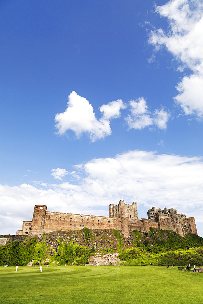 Bamburgh Castle, a medieval fortress, Grade I Listed Building constructed on top of a craggy outcrop of volcanic dolerite, overlooking a cricket ground, Bamburgh, Northumberland, England, United Kingdom, Europe