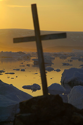 Cross in front of sunset over icebergs Paarnakajiit Sermilik Fjord Eastgreenland