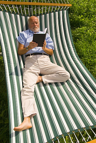 Elderly gentleman lying in a hammock reading a book