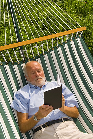 Elderly gentleman lying in a hammock reading a book